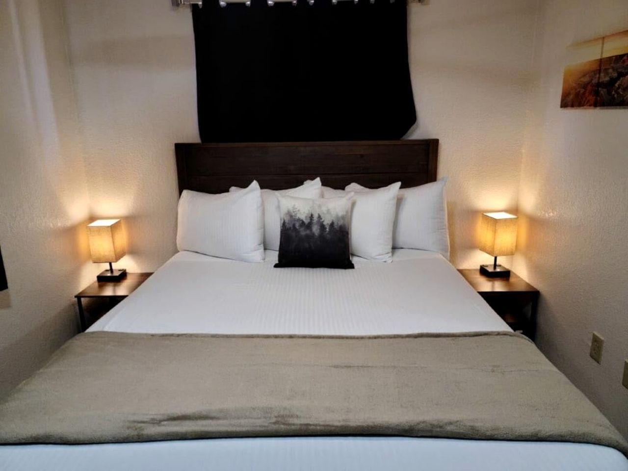 Una cama con cabecera, dos mesitas de noche con lámparas, y una sola almohada con estampado de bosque.