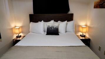 Una cama con cabecera, dos mesitas de noche con lámparas, y una sola almohada con estampado de bosque.