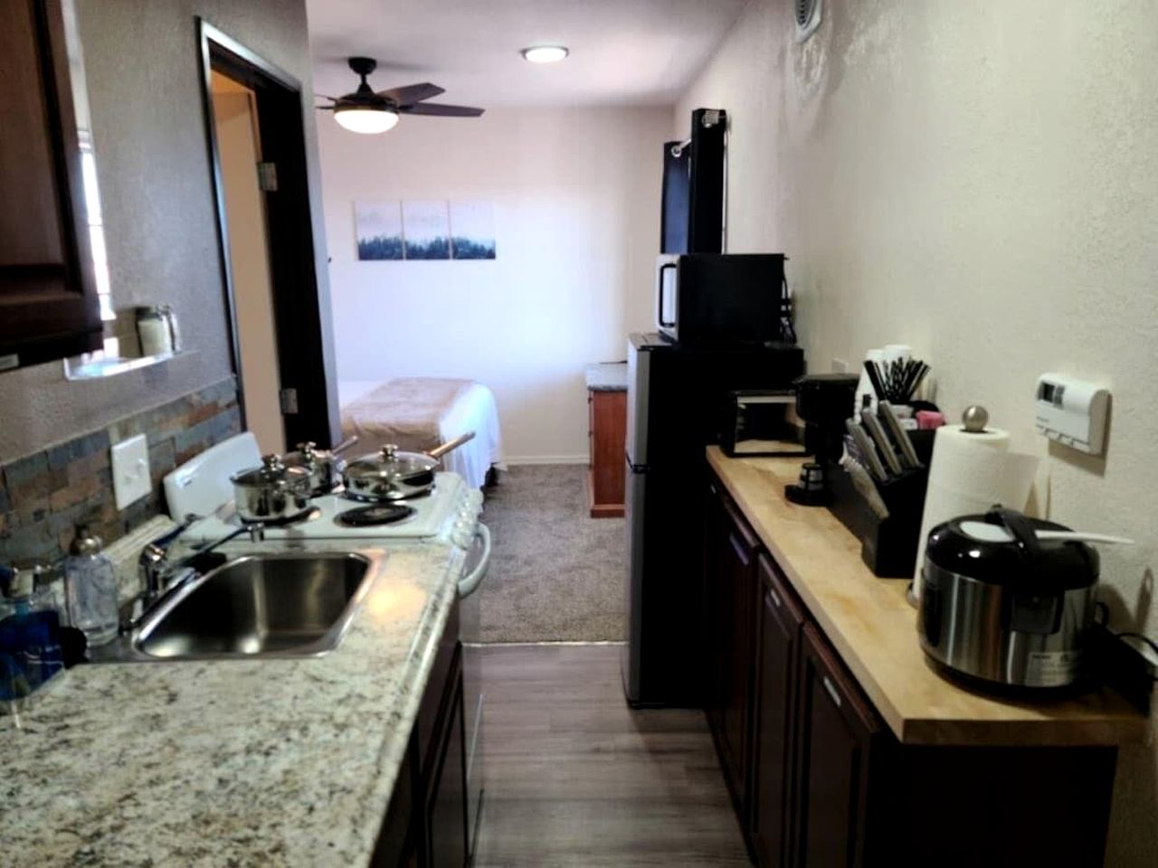 A compact kitchen with granite countertops, a sink, a stove, a microwave, and a coffee maker.