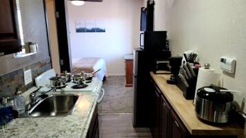 A compact kitchen with granite countertops, a sink, a stove, a microwave, and a coffee maker.