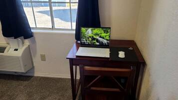 Um quarto pequeno com uma escrivaninha, um laptop, uma janela com cortinas e um aquecedor.