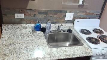A kitchen with granite countertops, a stainless steel sink, a white stove, and wooden cabinets.