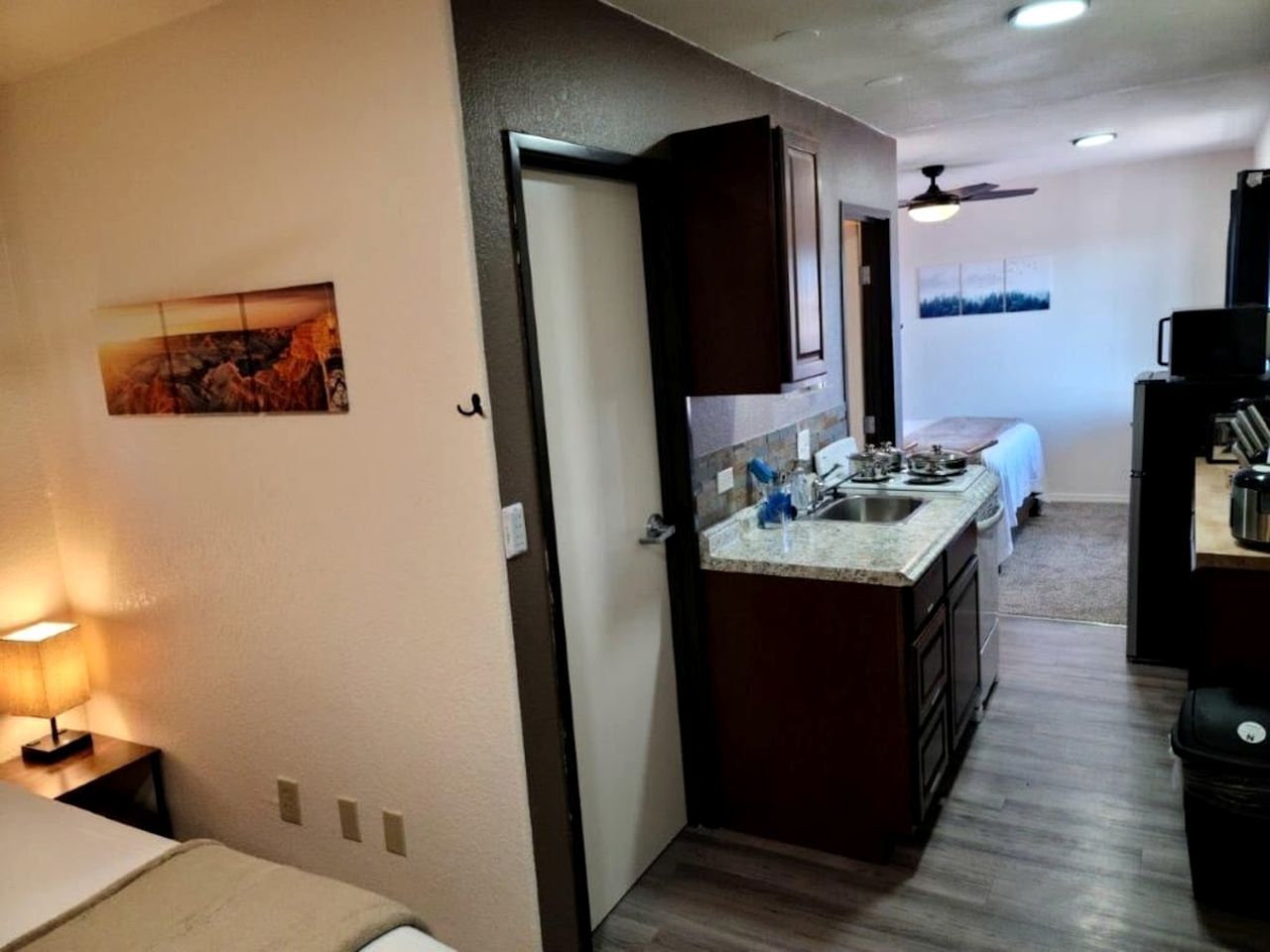 Una cocina compacta con una isla central, una zona de comedor con mesa y sillas, y un dormitorio con cama.