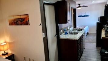 Una cocina compacta con una isla central, una zona de comedor con mesa y sillas, y un dormitorio con cama.