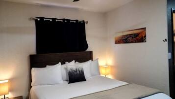A hotel room with a bed, a ceiling fan, a nightstand, a lamp, and a painting on the wall.