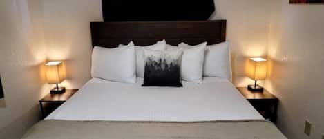 A bed with a headboard, two bedside tables with lamps, and a single pillow with a forest print.