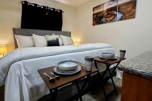 Een hotelkamer met een bed, nachtkastjes, een kleintje tafeltje met borden en kopjes, en een schilderij aan de muur.