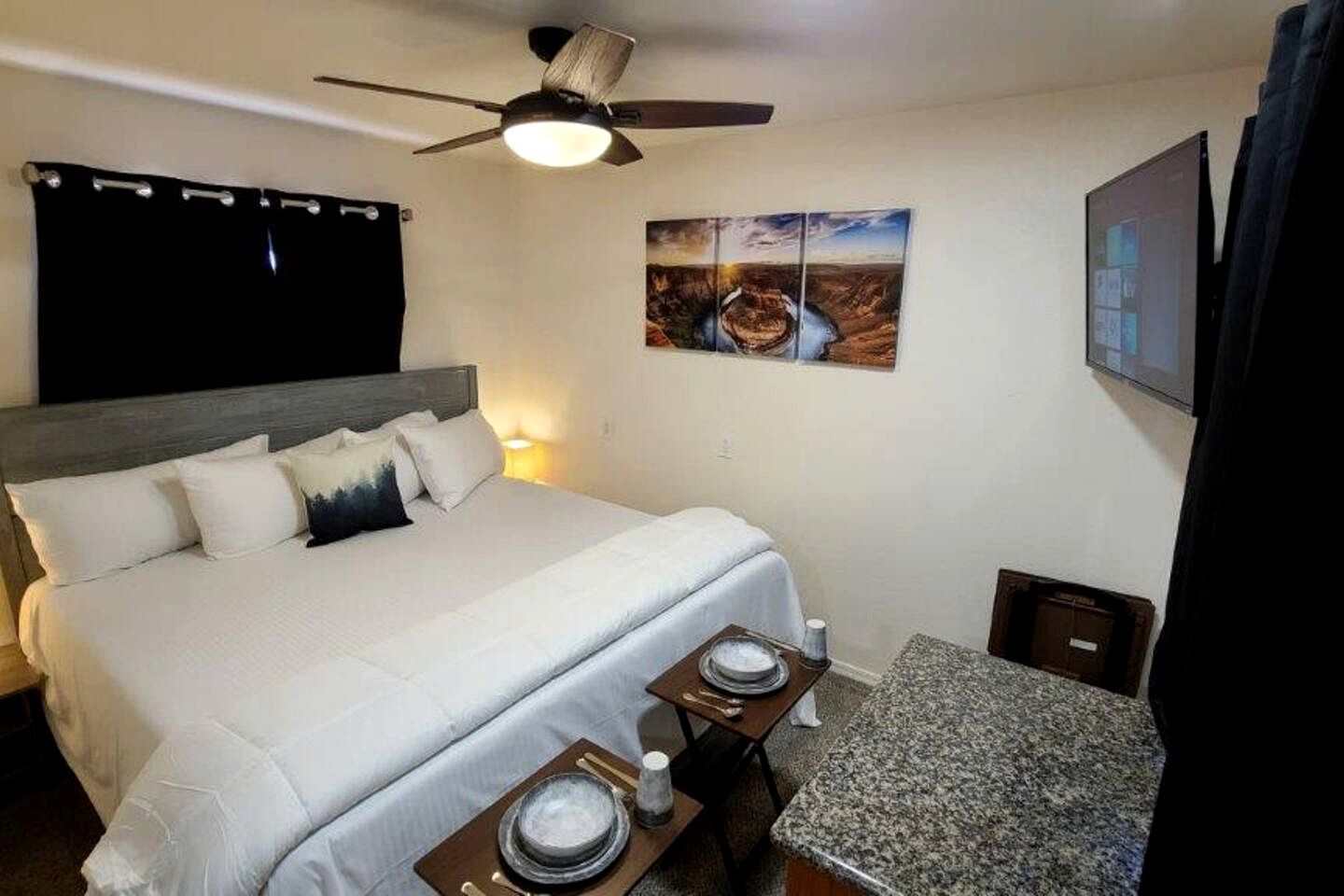 Une chambre d’hôtel avec un lit, un ventilateur de plafond, un tableau, une télévision et une petite table avec un plateau.