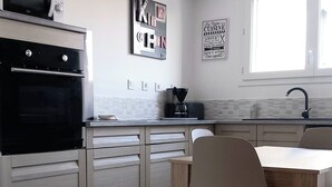 Eine moderne Küche mit Einbauofen, Esstisch mit Stühlen, einer Kaffeemaschine und einem Fenster.