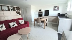 A compact living space with a kitchenette, a dining area, and a red sofa with decorative pillows. - Cosy, fully-equipped studio renovated to a high standard Amenities on foot, beach only 3 kms away (Plouhinec)