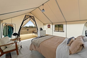 A tented accommodation with a bed, seating area, and a view of the outdoors.