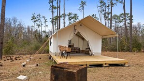 A tent with a wooden deck, two chairs, and a table set up in a forested area.