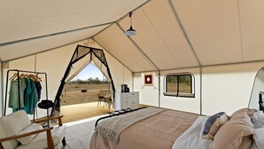 A tented accommodation with a bed, seating area, and a view of the outdoors.