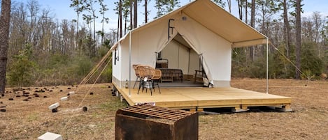 Ein Zelt mit Holzterrasse, zwei Stühlen und einem Tisch in bewaldeter Landschaft.