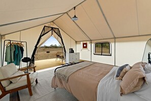 A tented accommodation with a bed, seating area, and a view of the outdoors.