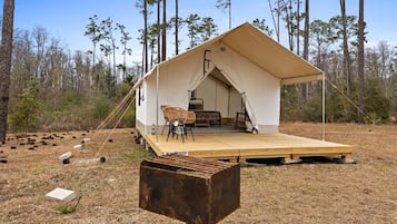 A tent with a wooden deck, two chairs, and a table set up in a forested area.