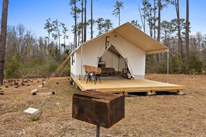 A tent with a wooden deck, two chairs, and a table set up in a forested area.