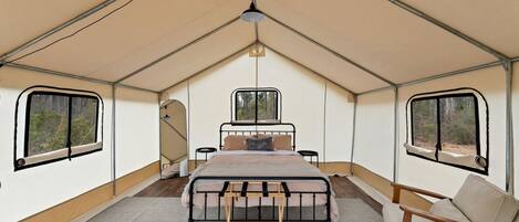 Una tenda trasformata in stanza con un letto, una sedia, un tavolino e una finestra.