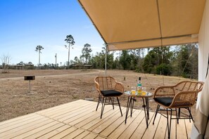 An outdoor patio with two wicker chairs, a small round table, and a bottle of liquor.
