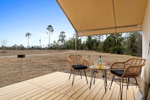 An outdoor patio with two wicker chairs, a small round table, and a bottle of liquor.