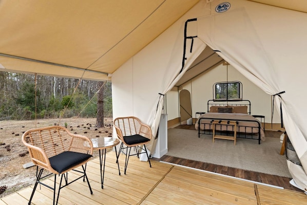 Alojamiento con carpa que incluye una cama, dos sillas, una mesa y vistas al bosque.