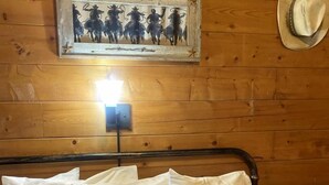 Ein Zimmer in einer Holzhütte mit einem Bett, weißen Kissen, einer gemusterten Decke, einem Wandbild und einem Hut an der Wand.