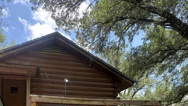 A rustic cabin with a covered grill area, two Adirondack chairs, and a wooden deck. - The Renegade in Bluff Dale, TX (Bluff Dale)