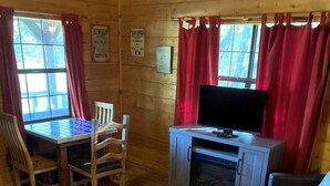 A wooden cabin interior with a dining table, chairs, a television, a sofa, and a fireplace. - The Renegade in Bluff Dale, TX (Bluff Dale)