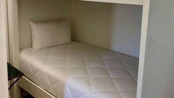 A bunk bed with a quilted mattress and pillows, a small table beside it, and a wooden floor.