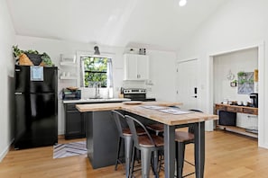 A modern kitchen with a central island, a black refrigerator, and a window with a view of greenery. - Beautiful Cabin with Deck and Hot Tub Overlooking Spring Creek in Texas (Fredericksburg)