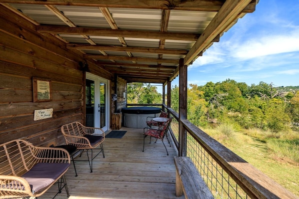 A wooden cabin with a porch, wicker chairs, a hot tub, and a view of the surrounding forest.
