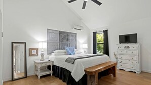 Un dormitorio con cama, mesitas de noche, un banco, cómoda y ventilador de techo.