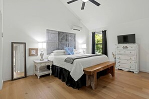 A bedroom with a bed, bedside tables, a bench, a dresser, and a ceiling fan. - Beautiful Cabin with Deck and Hot Tub Overlooking Spring Creek in Texas (Fredericksburg)