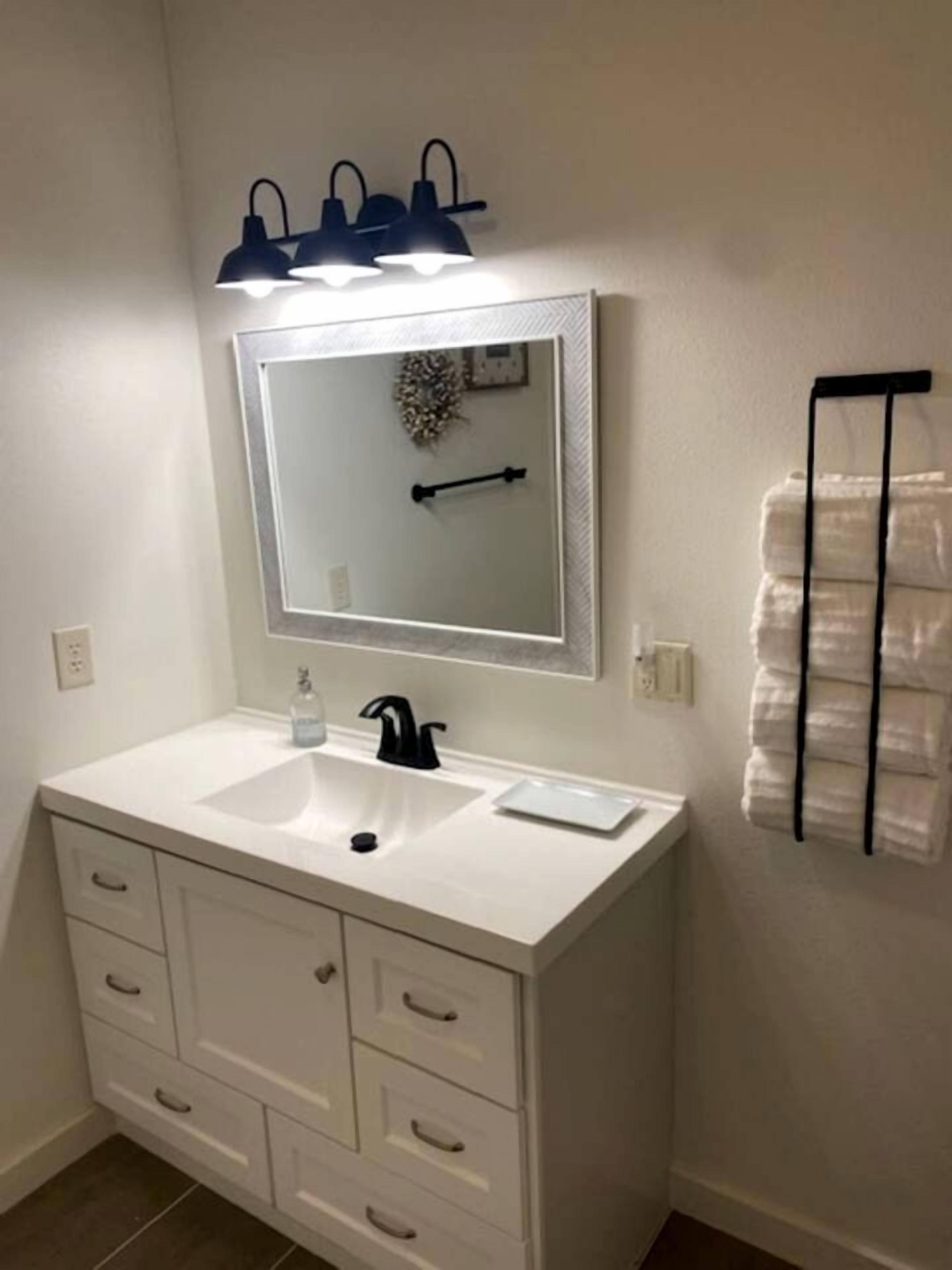 A bathroom with a white vanity, a mirror, a black faucet, and a towel rack.