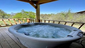 Un jacuzzi en una terraza de madera con vistas despejadas a árboles y un edificio al fondo.