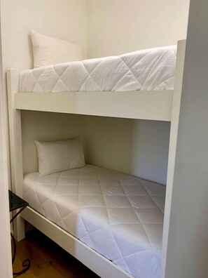 A bunk bed with a quilted mattress and pillows, a small table beside it, and a wooden floor. - Beautiful Cabin with Deck and Hot Tub Overlooking Spring Creek in Texas (Fredericksburg)