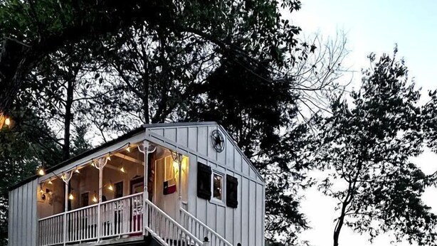A cabin with a staircase leading to a deck, surrounded by trees. - Unique Treehouse on Working Farm in Texas, Perfect for Rustic Weekends in Nature (Forestburg)