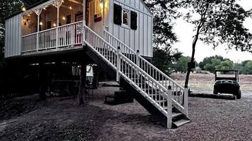 Une cabane avec un escalier menant à une terrasse, le tout entouré d’arbres.