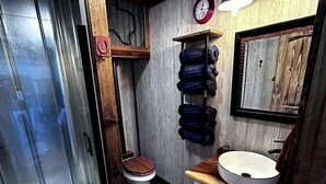 A bathroom with a glass shower enclosure, a wooden vanity with a sink, and a towel rack. - Unique Treehouse on Working Farm in Texas, Perfect for Rustic Weekends in Nature (Forestburg)