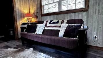 Ein Zimmer mit Holzbalkendecke, einem großen Fenster, einer Couch mit Decke und einem Teppich.
