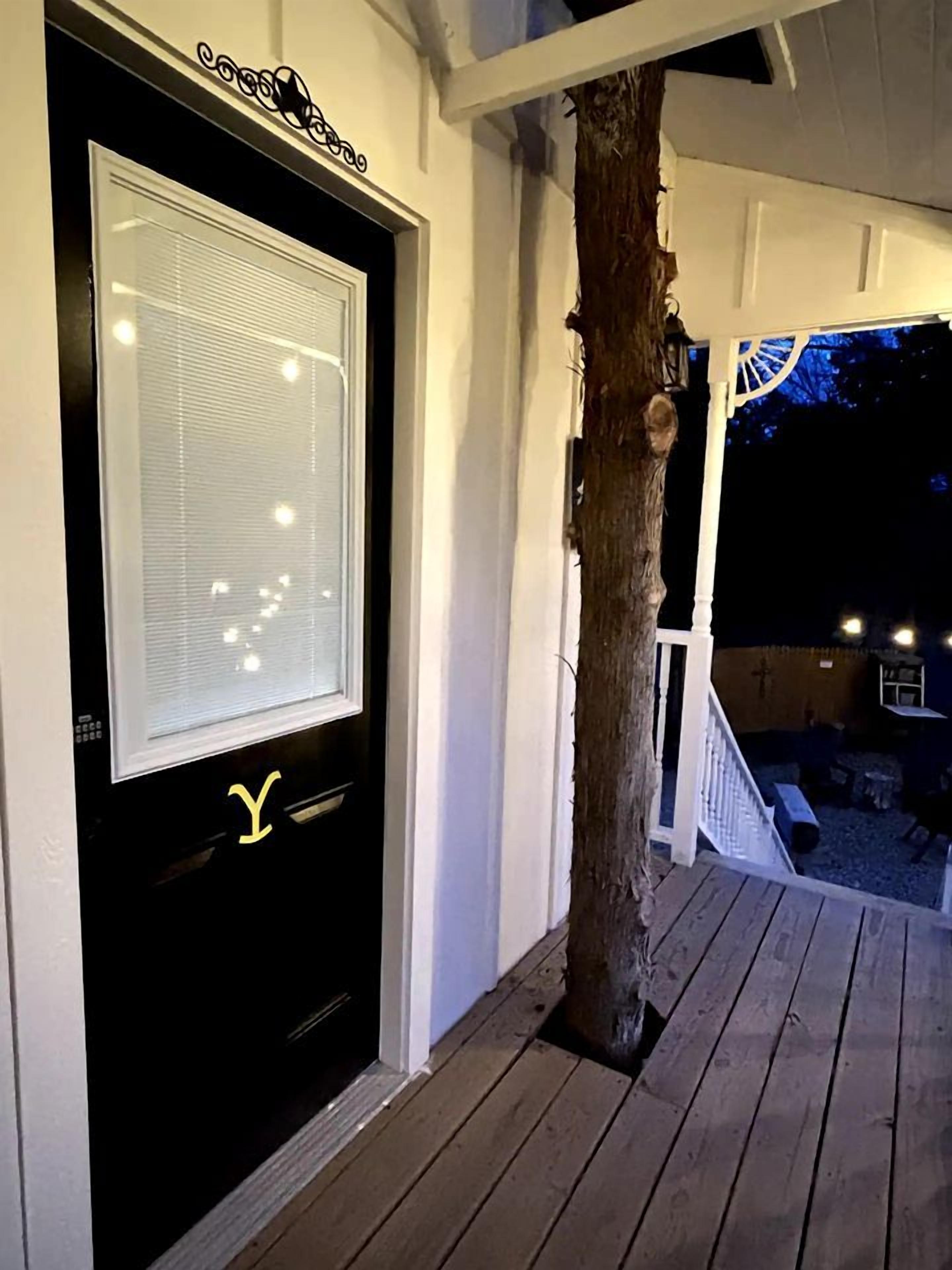 Une terrasse en bois avec une porte blanche dotée d’une fenêtre et ornée d’un symbole jaune en forme de « Y ».