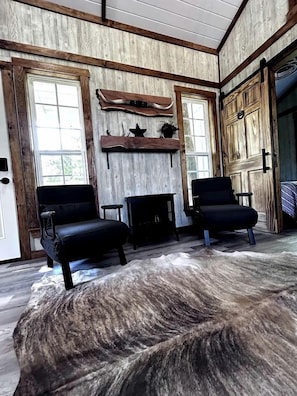 A room with wooden walls, a large fur rug, two black chairs, a fireplace, and a wooden door.