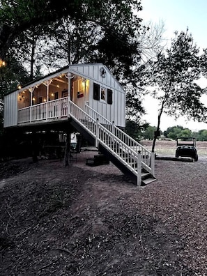 A cabin with a staircase leading to a deck, surrounded by trees.