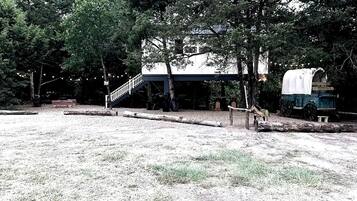 A rustic cabin with a covered porch, a staircase, and a covered wagon.