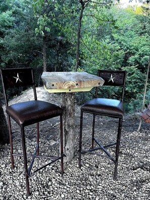 A rustic outdoor seating area with two chairs and a table, surrounded by gravel and greenery.
