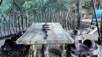 Une table en bois rustique, placée sous un toit en tôle ondulée, et entourée de selles en cuir et d’autres équipements équestres.