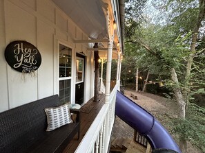 A porch with a dark-colored sofa and a cushion, a 'Hey y'all' sign, and a blue slide.