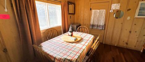Une pièce aux murs lambrissés, avec une table dressée pour deux personnes, une horloge au mur et une porte sur laquelle est apposée une pancarte.