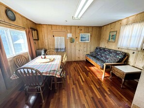 Ein Interieur einer Holzhütte mit Esstisch, Stühlen, einer Couch, Holzwänden und einer Deckenleuchte.