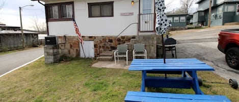 Ein kleines Haus mit einer Steinfassade, einem blauen Picknicktisch und einer US-amerikanischen Flagge.